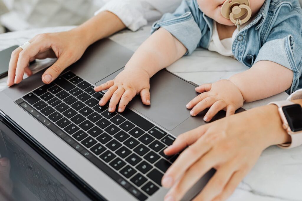 Mama z niemowlakiem przy laptopie sprawdzają, gdzie szukać pracy zdalnej