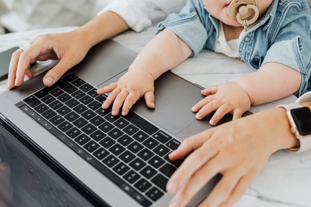 Mama przy laptopie z dzieckiem planuje powrót do pracy po urlopie macierzyńskim