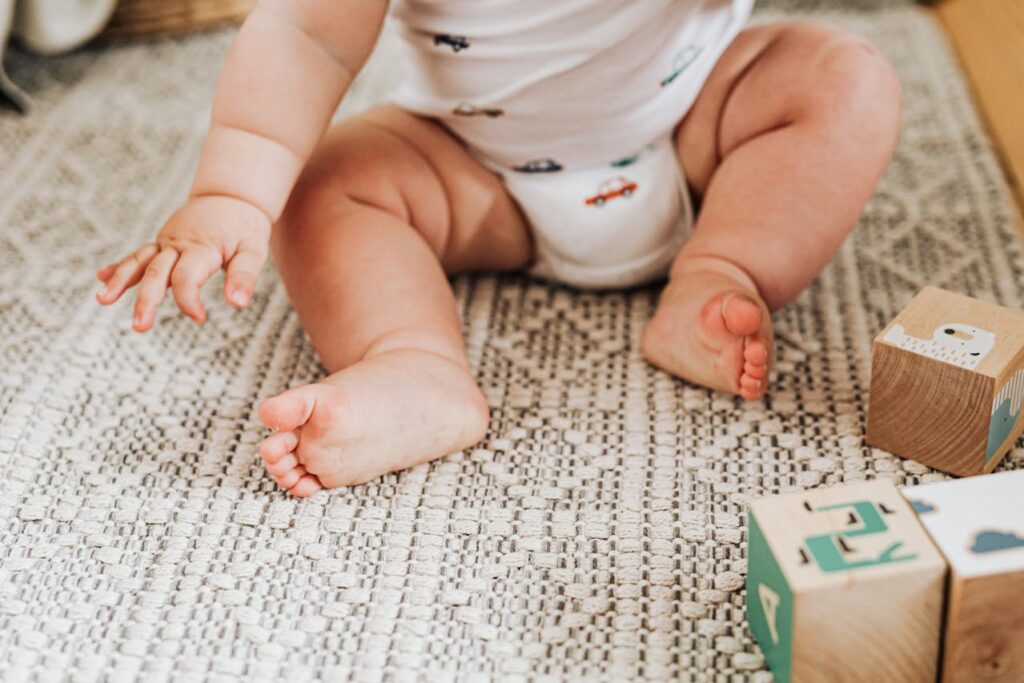 odpieluchowanie dziecka: dziecko w pieluszce siedzi na dywanie, obok klocki