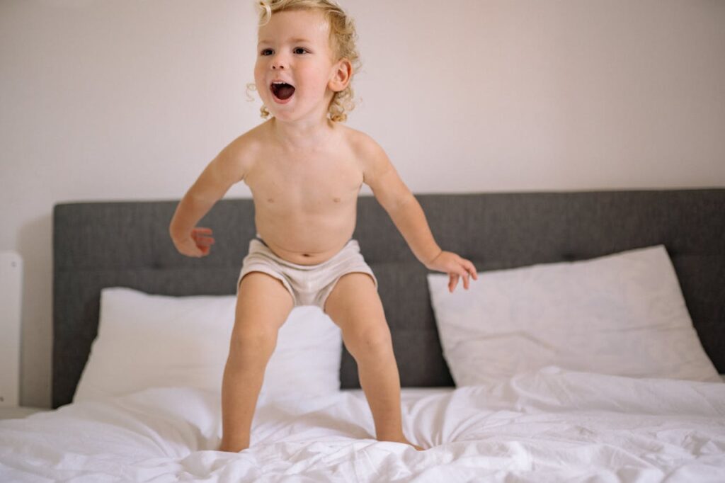 dziecko w pieluszce skacze po łóżku.