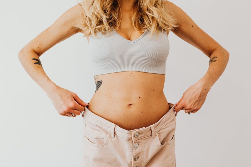 jak schudnąć po ciąży - kobieta z odkrytym brzuchem trzyma po bokach nieco za duże spodnie