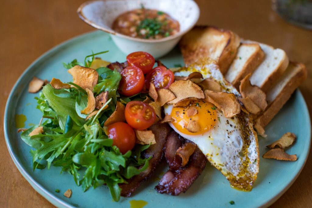błękitny talerz z jajkiem, boczkiem, tostami, pomidorkami koktajlowymi i sałatą jako przykład zdrowego posiłku
