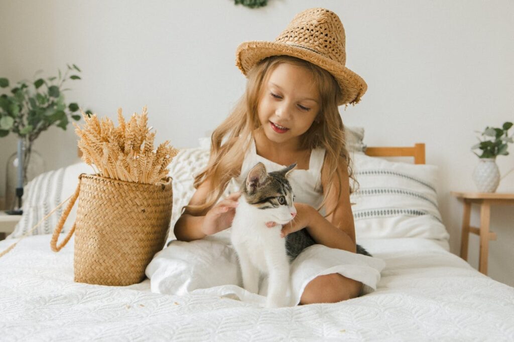 dziewczynka siedzi na łóżku z kotem i go głaszcze. 