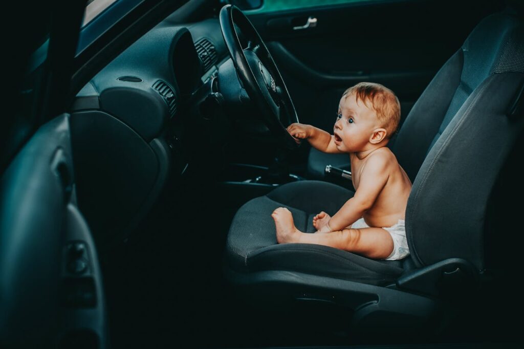 niemowlę siedzi na przednim siedzeniu w samochodzie i dotyka kierownicy