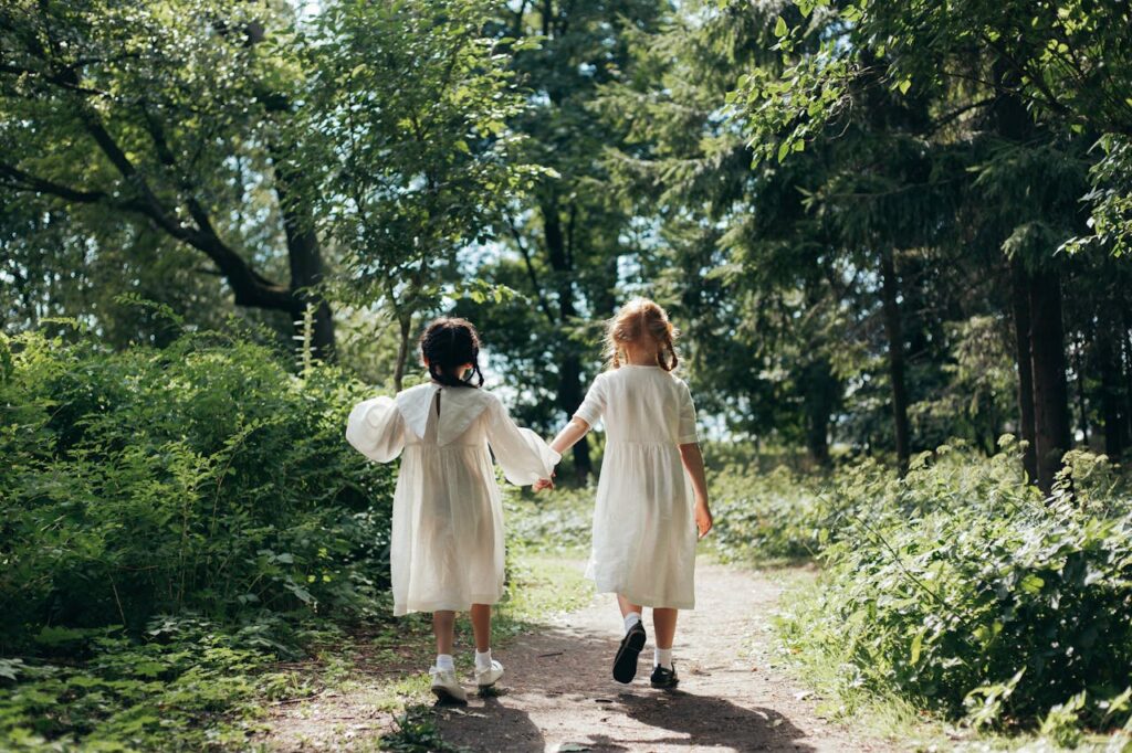 dwie dziewczynki spacerują po ścieżce w lesie podczas wiosennej sesji zdjęciowej