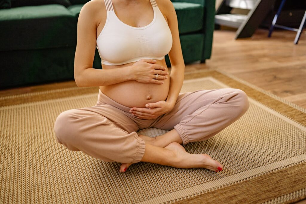 kobieta w drugim trymestrze ciąży siedzi na macie do ciąży po turecku i obejmuje dłońmi brzuch